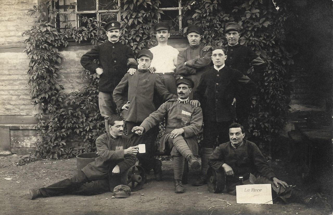 Des prisonniers italiens se font photographier dans une usine de Graffenstaden pour immortaliser leur exil : Settimio Damiani est parmi eux (debout, le deuxième à partir de la gauche) │ Carte postale non circulée │ col. pdgit1918