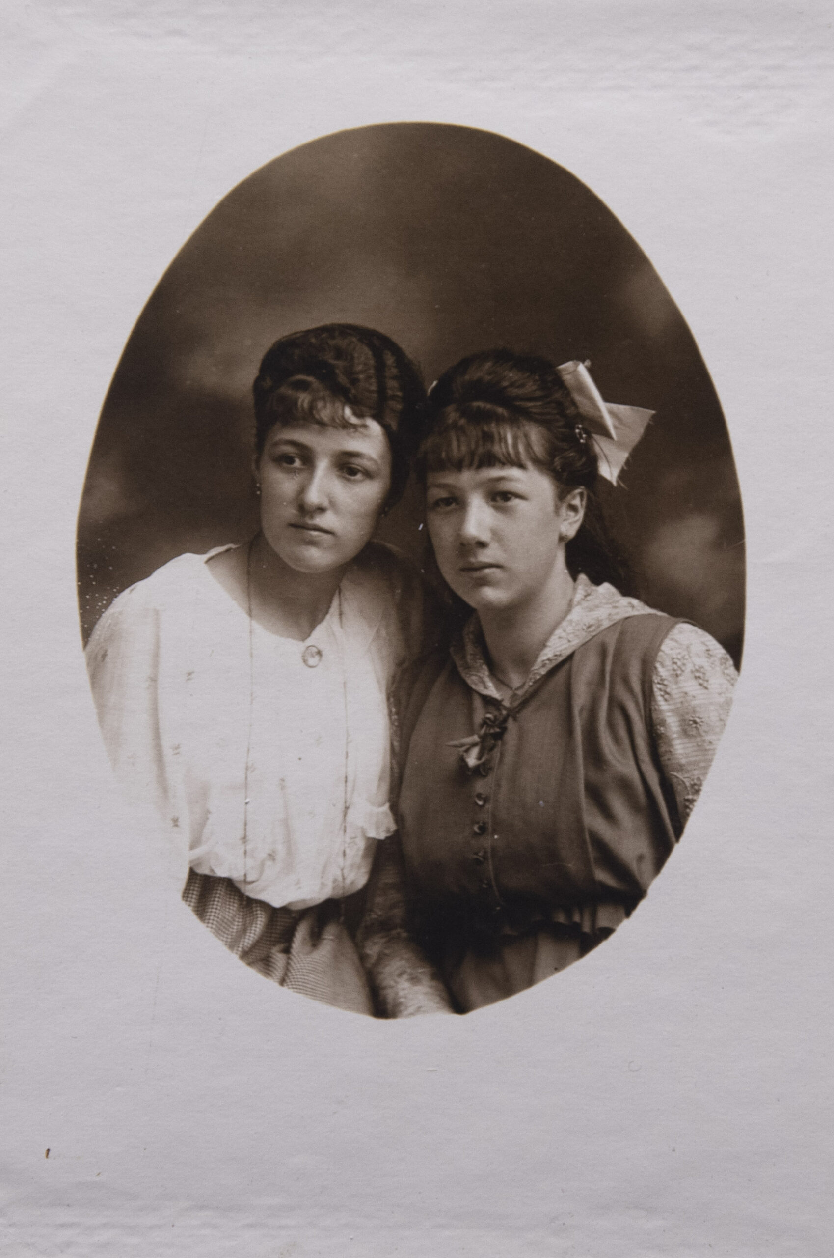 Portrait de deux marraines, présentes sur la photographie suivante (celle de droite est debout avec un nœud noir dans les cheveux et celle de gauche est assise au sol en tailleur, portant une tirelire)